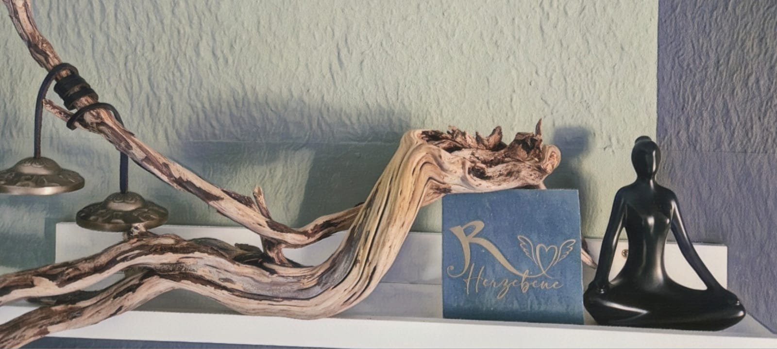 Decorative shelf display with twisted driftwood, blue book, black meditation figurine, and pendant lights against a white wall