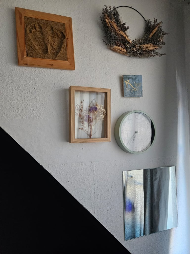 White wall displaying home decor including framed pressed flowers, dried wreath, abstract paintings, and a wall clock