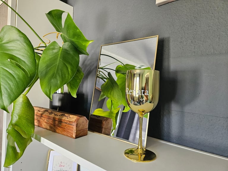 A shelf displaying potted green plants, a wooden planter, a mirror, and a yellow glass candle holder against a gray wall.